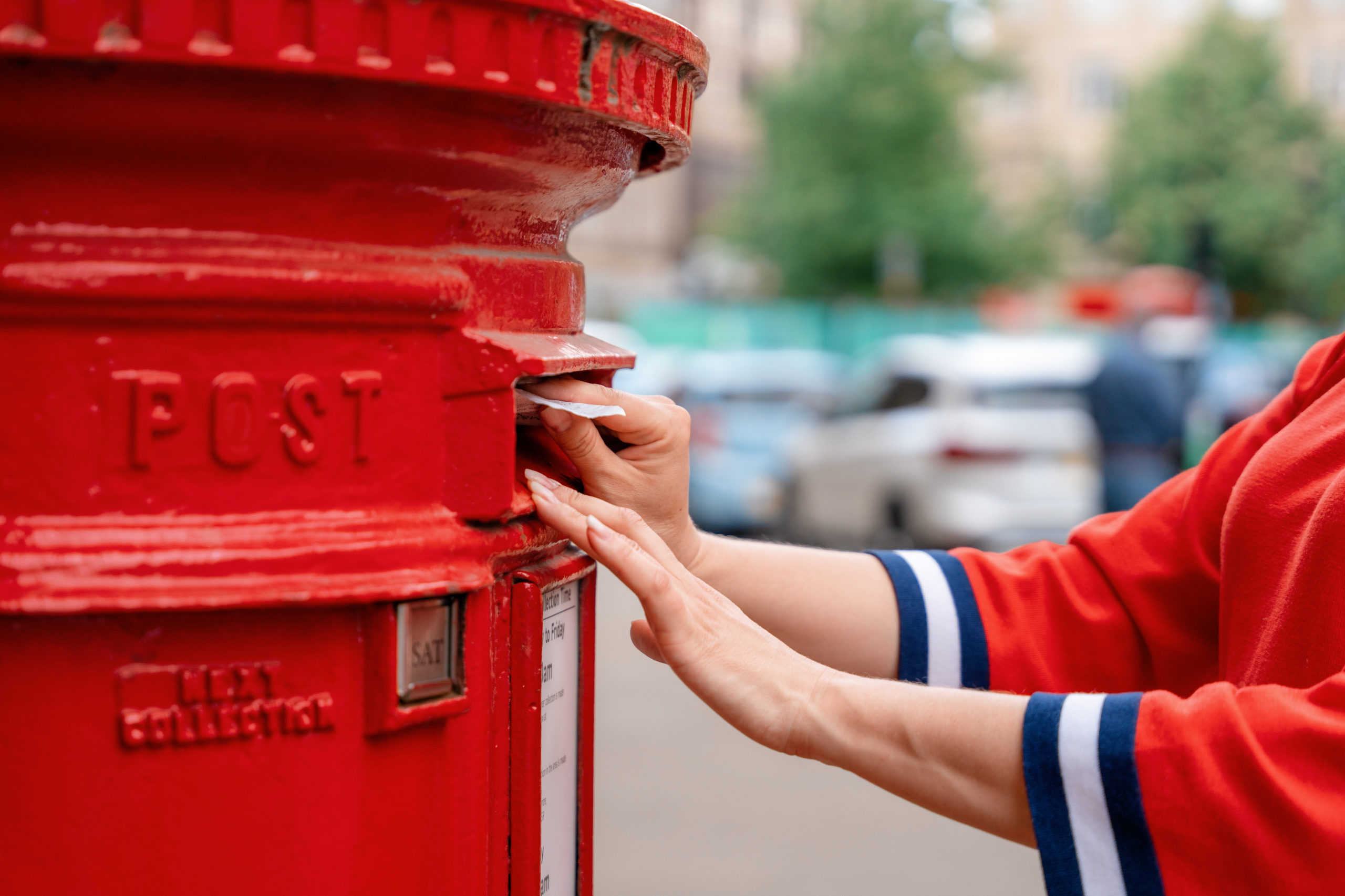 woman posting letters in red post box in England
