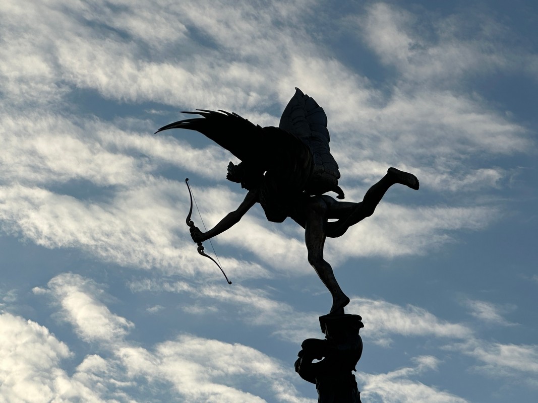 Set against a backdrop of a partly cloudy London sky, the silhouette of a winged statue clutching a bow evokes a sense of dynamic grace, as if leaping into flight. This iconic scene marks an ideal start to any Christian tour exploring the citys rich heritage and spiritual sites.