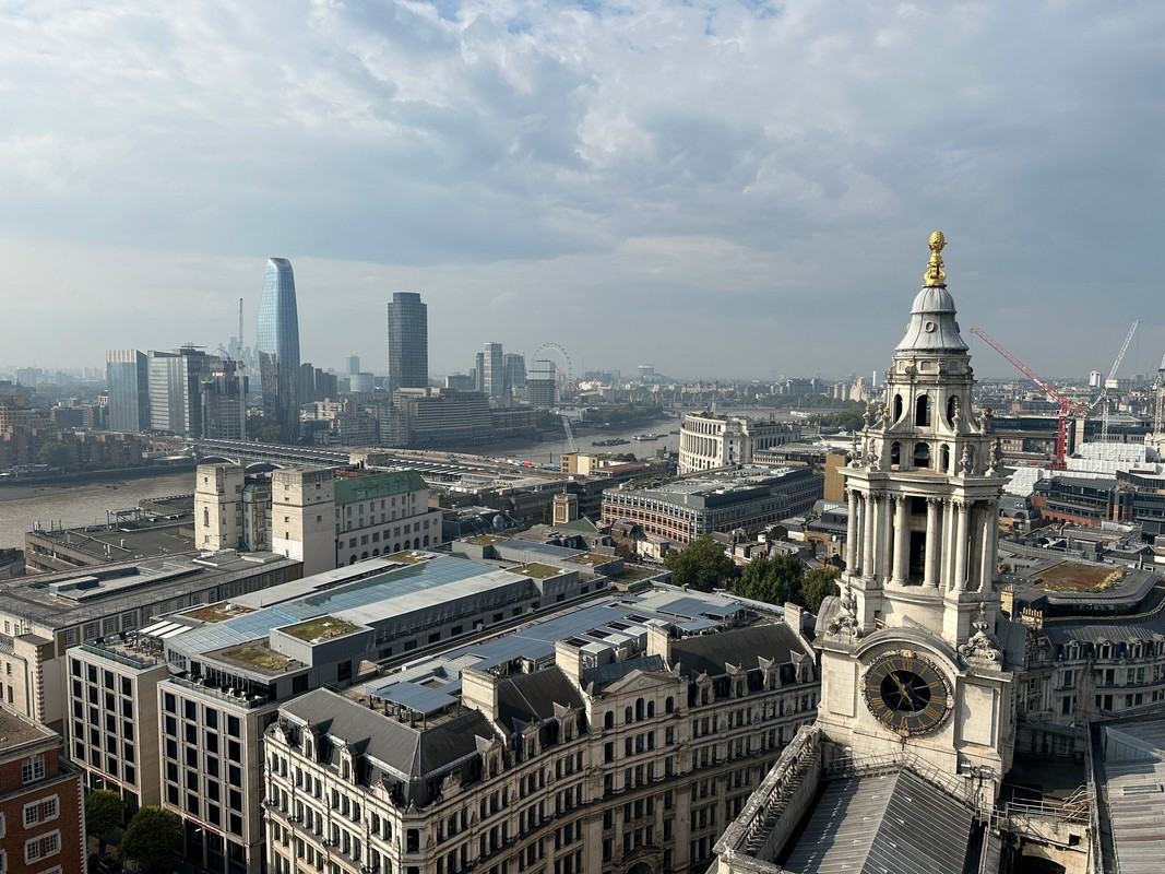 A panoramic view of Londons skyline reveals historic buildings in the foreground and modern skyscrapers rising behind. The Thames River elegantly winds through the city, while the London Eye stands visible in the distance under a partly cloudy sky, inviting exploration during a London Christian Tour.