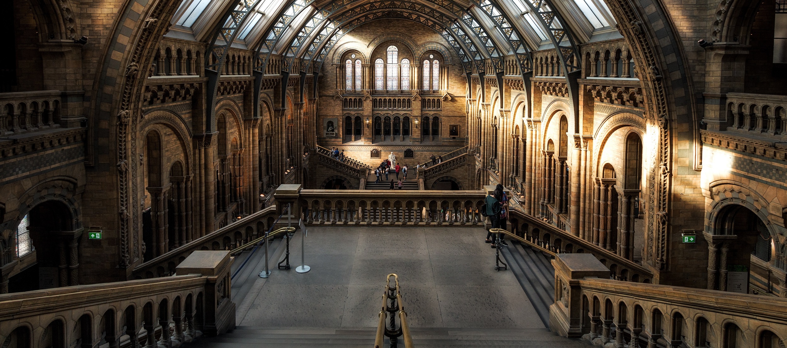 The interior of this grand, historic building, often featured in the tour itinerary, boasts arched windows and ornate stonework. A majestic staircase leads to a balcony, with sunlight streaming through the upper windows to highlight the exquisite architectural details on the walls and ceiling.