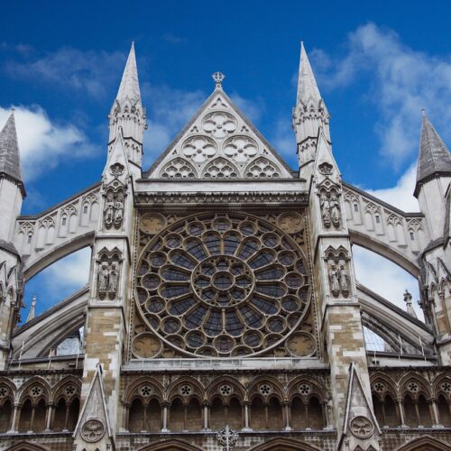 The image shows the ornate facade of a Gothic cathedral, perfectly capturing a highlight of any tour itinerary, with pointed spires and a large circular stained glass window. The detailed architecture features intricate stone carvings and arches, set against a clear and bright sky.