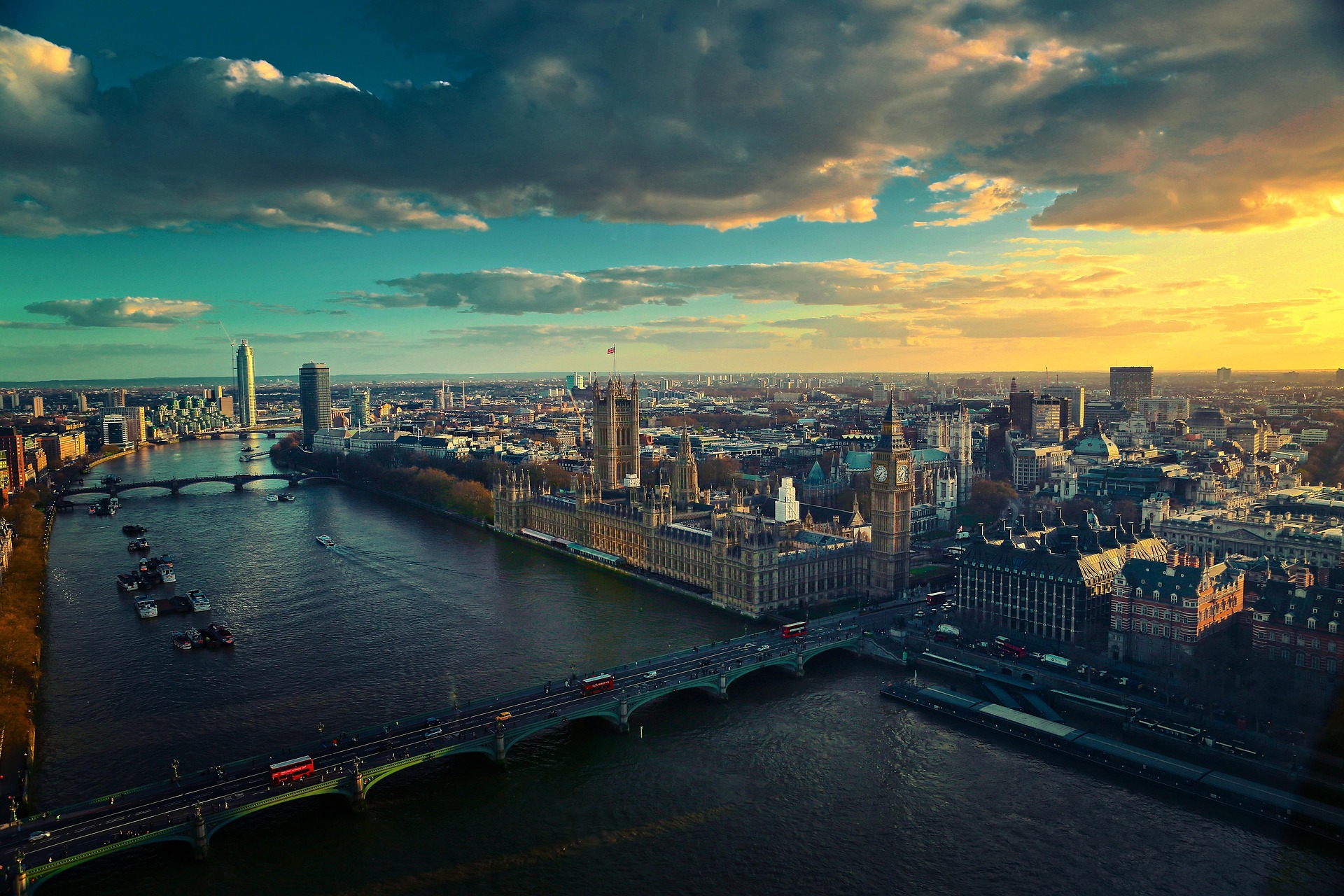Aerial view of London at sunset, showcasing the River Thames, Westminster Bridge, and the Houses of Parliament. The sky is partly cloudy, with the sun casting warm hues over the cityscape—a breathtaking sight for any traveler pondering their trip FAQs.