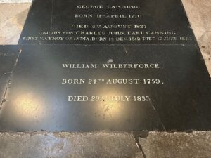 A stone memorial plaque engraved with the name William Wilberforce, noting his birth and death dates. The text is etched in capital letters on dark stone.
